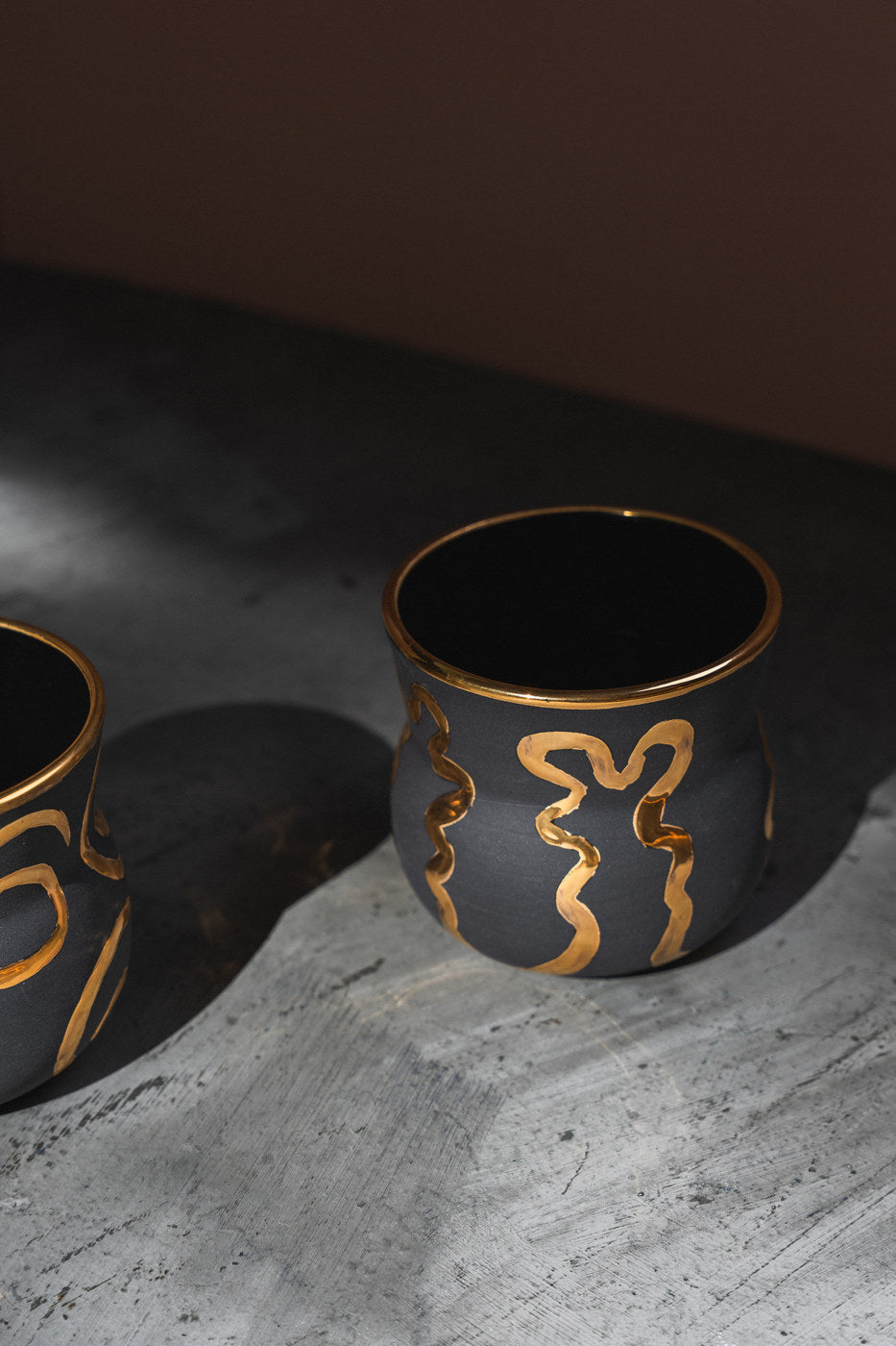 Black porcelain cups with hand-painted gold patterns in soft window light.