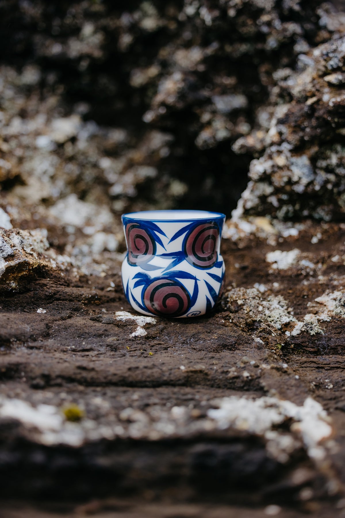 Hand-painted blue and rose Veltibolli porcelain cup on volcanic rock in Grindavík, Iceland.